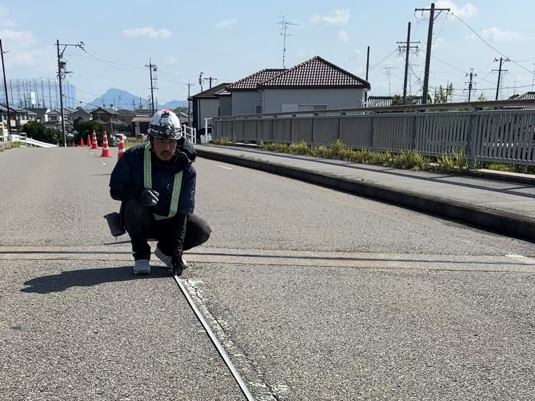 道路にしゃがみ路面の位置を確認する作業員